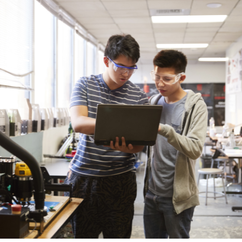 Students smiling while working on a laptop in class